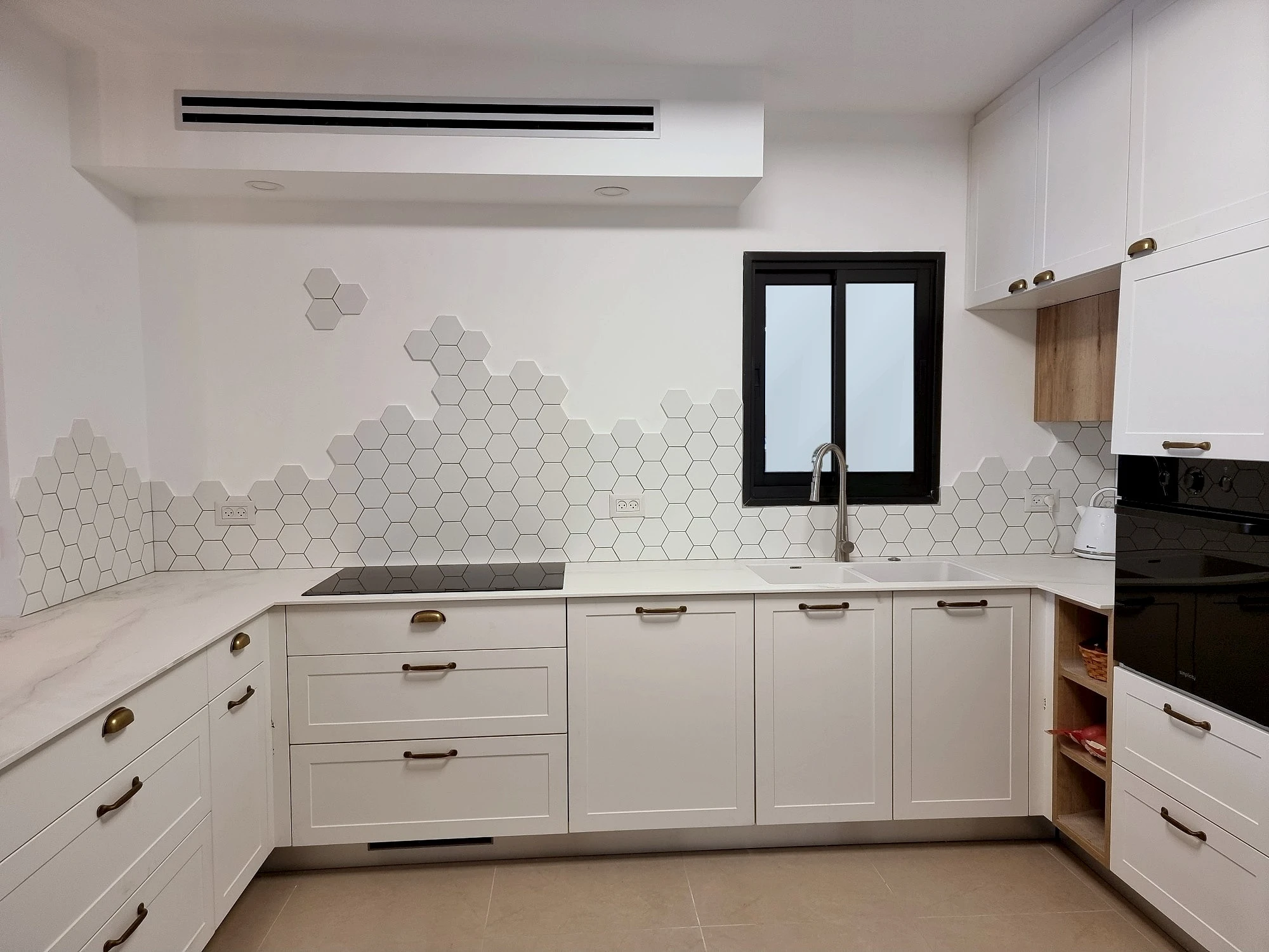 מטבח לבן בצורת פי עם קיר משושים, חלון שחור וידיות פליז עתיקות