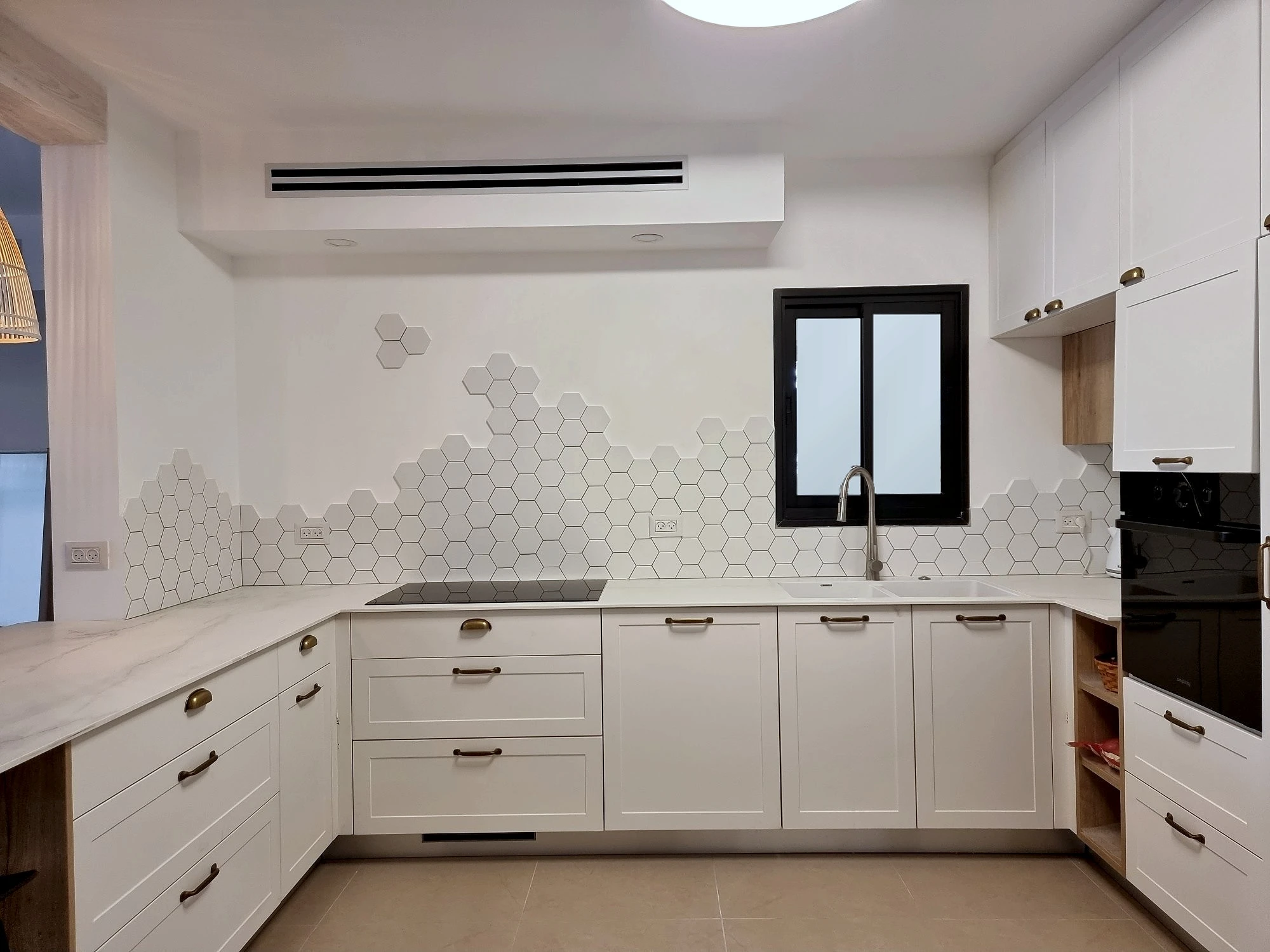 המטבח המוגמר מרחוק, עם גוף תאורה עגול בתקרה ואי הישיבה בצד