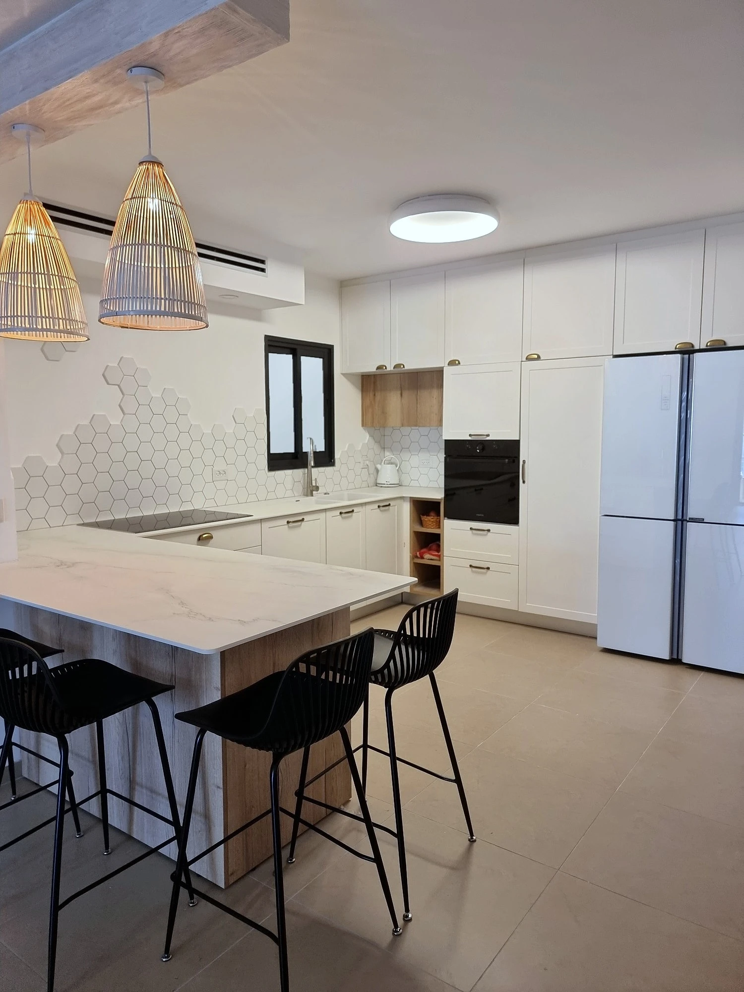 מבט על המטבח עם מקרר דלתות לבן בקצה, חצי האי וכסאות הבר השחורים