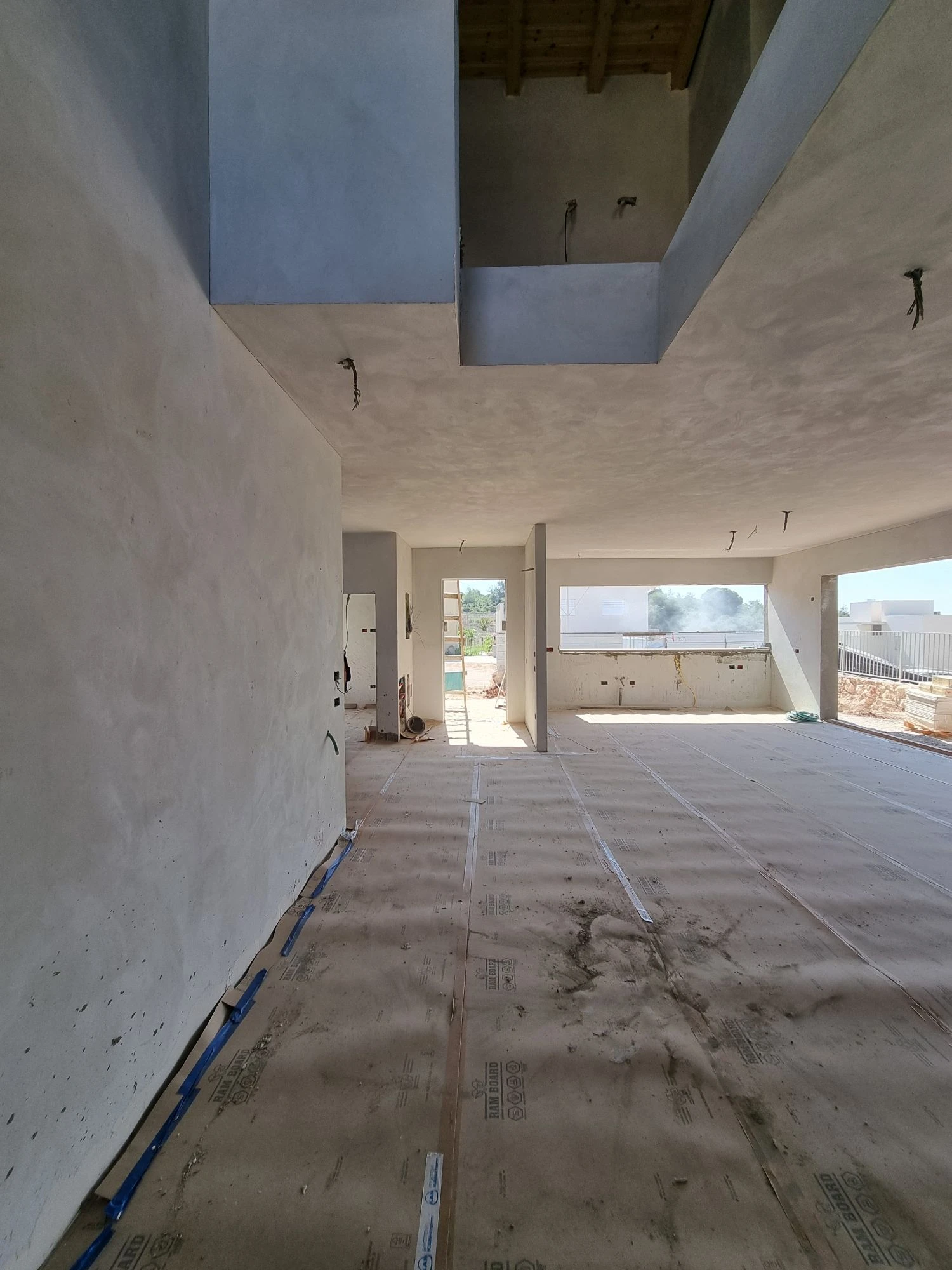 קומת המגורים הפתוחה בשלב הטיח, עם רצפה מכוסה בלוחות הגנה וחלל כפול גובה