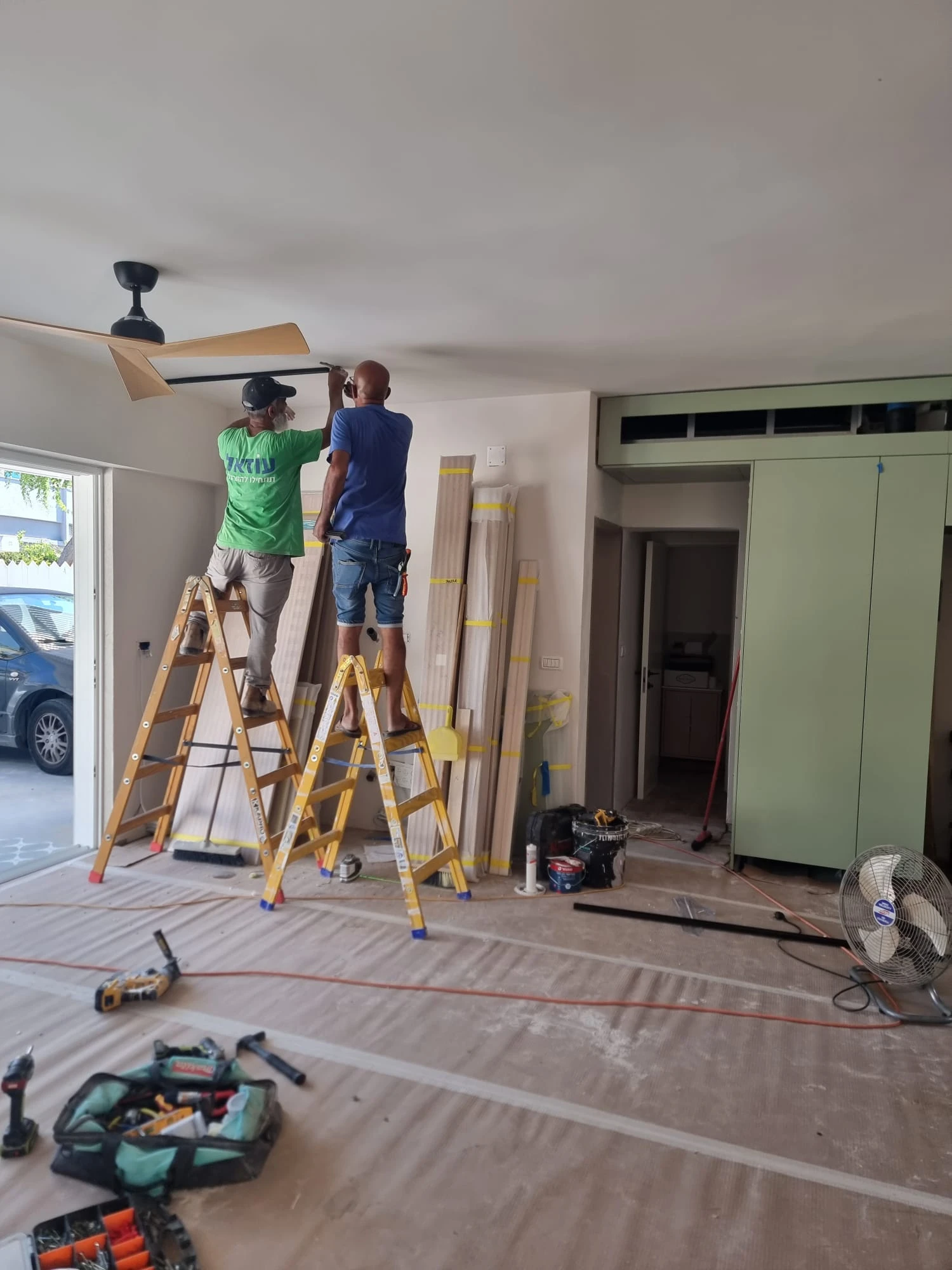 שני נגרים מתקינים מאוורר תקרה וגוף תאורה בסלון