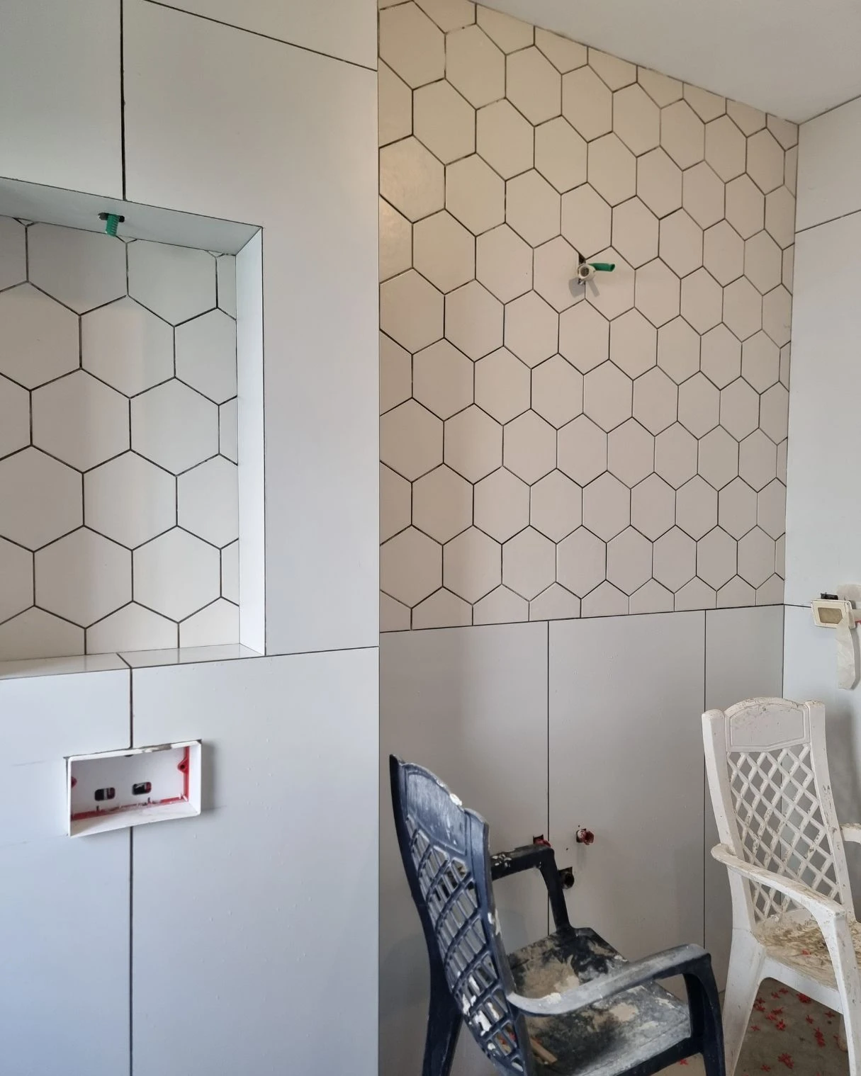 קיר מחופה באריחים משושים לבנים עם נישה בזמן השיפוץ