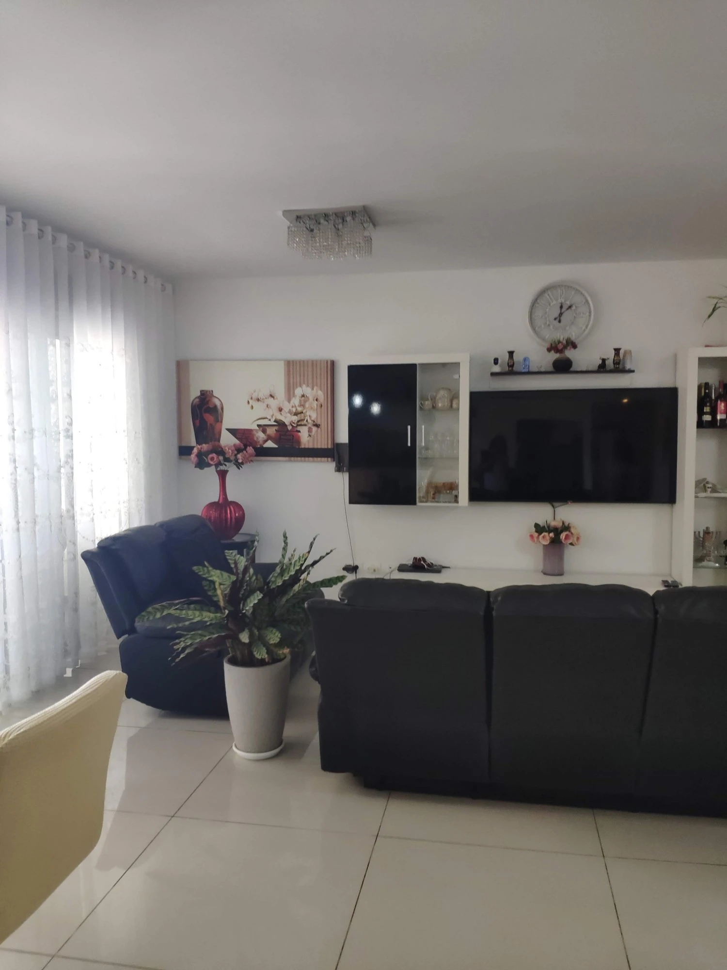 סלון וקיר הטלוויזיה לפני השיפוץ, עם וילון לבן וכורסת עור