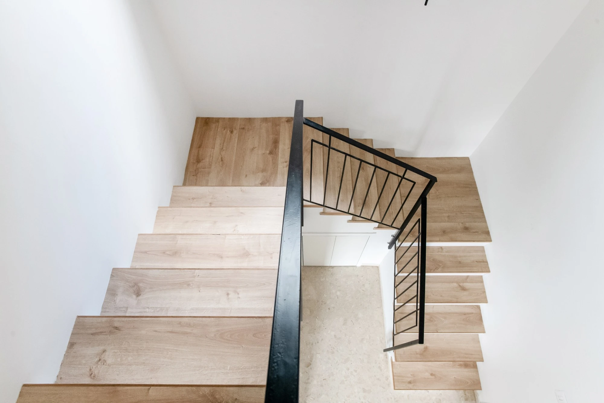מדרגות עץ ומעקה שחור בפיתול, וארון חבוי ורצפת טרצו למטה